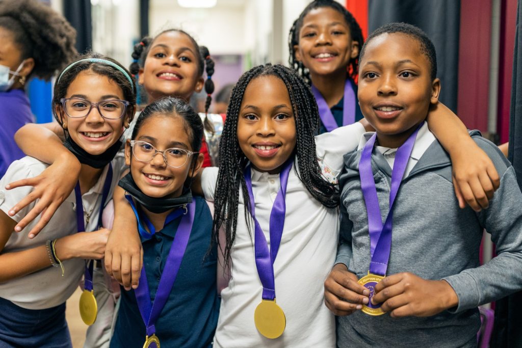 a group of students smile while holding medals on purple ribbons