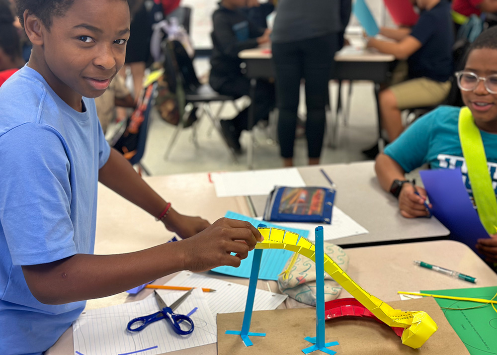 Two students work at a table on a paper roller coaster