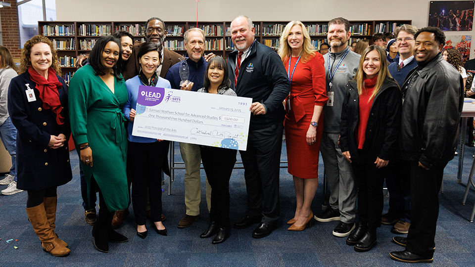 A group of adults hold a giant check and the principal of the arts award for 2025, awarded to Christopher Begley of Wolfson High