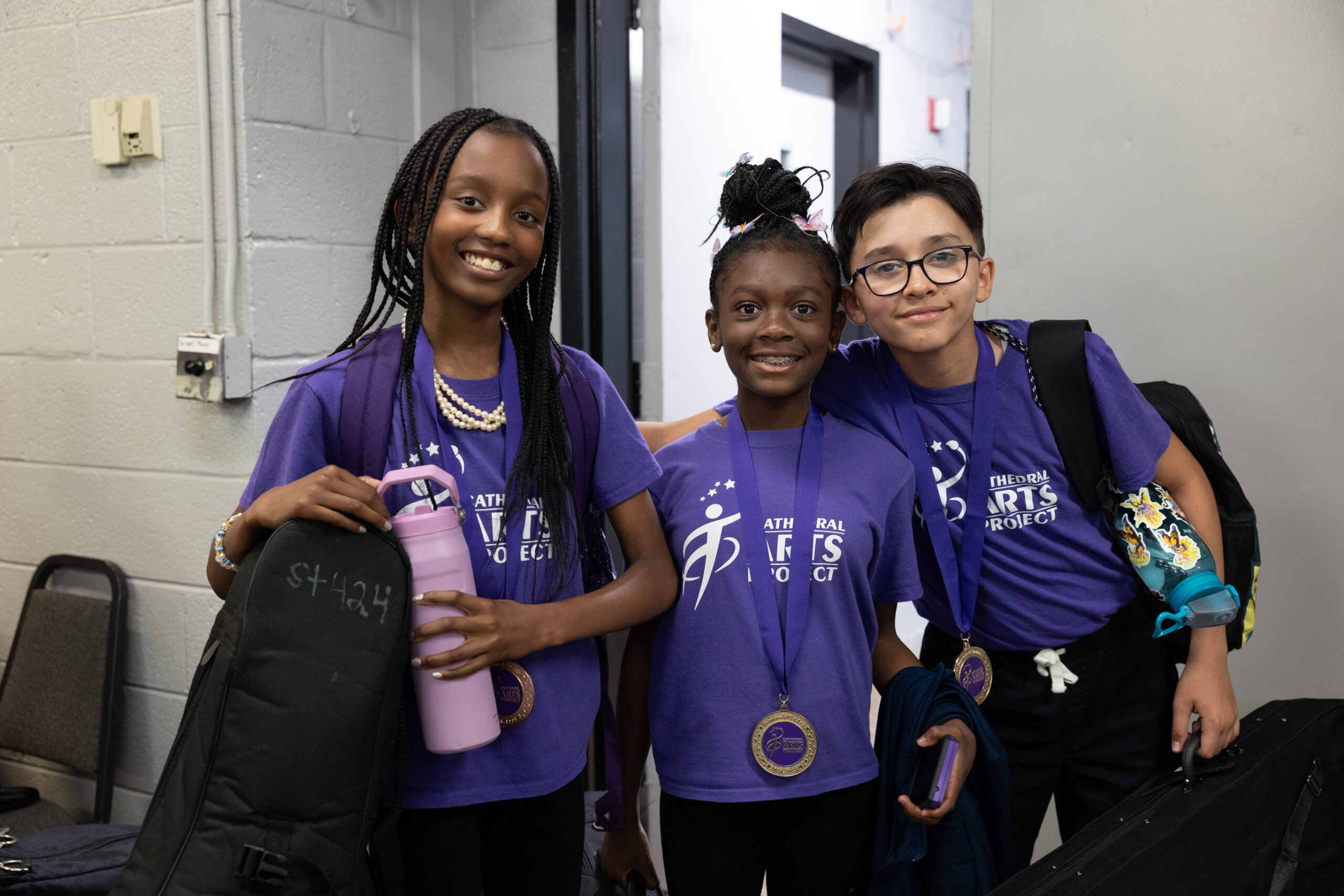 three CAP students in purple shirts holding instrument bags