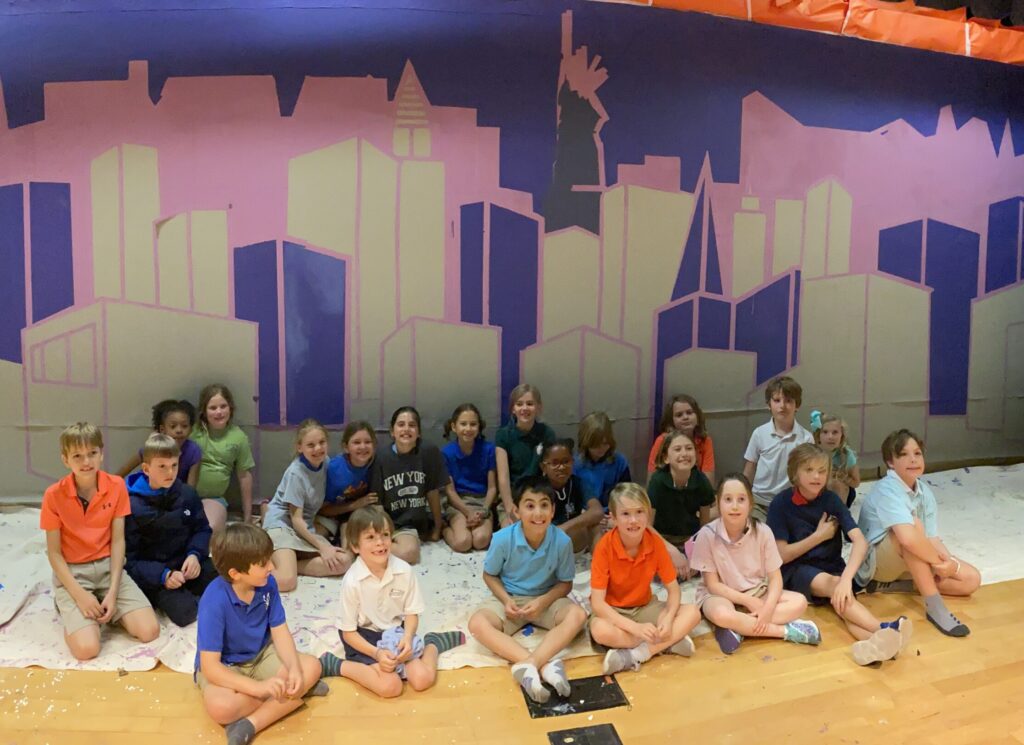 Students sitting in front of a mural they are painting as a team